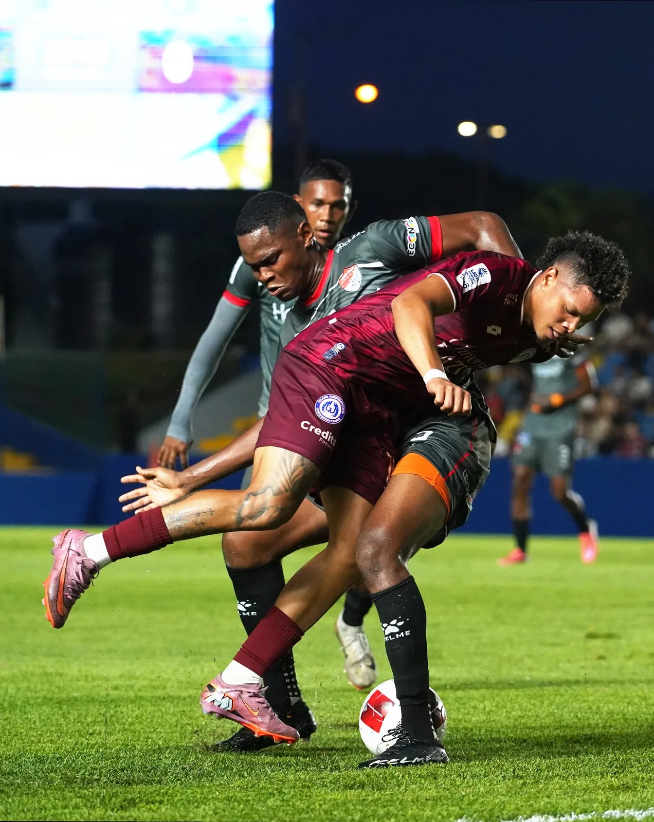 Dos jugadores chocan hombro con hombro por el balón en un partido de noche