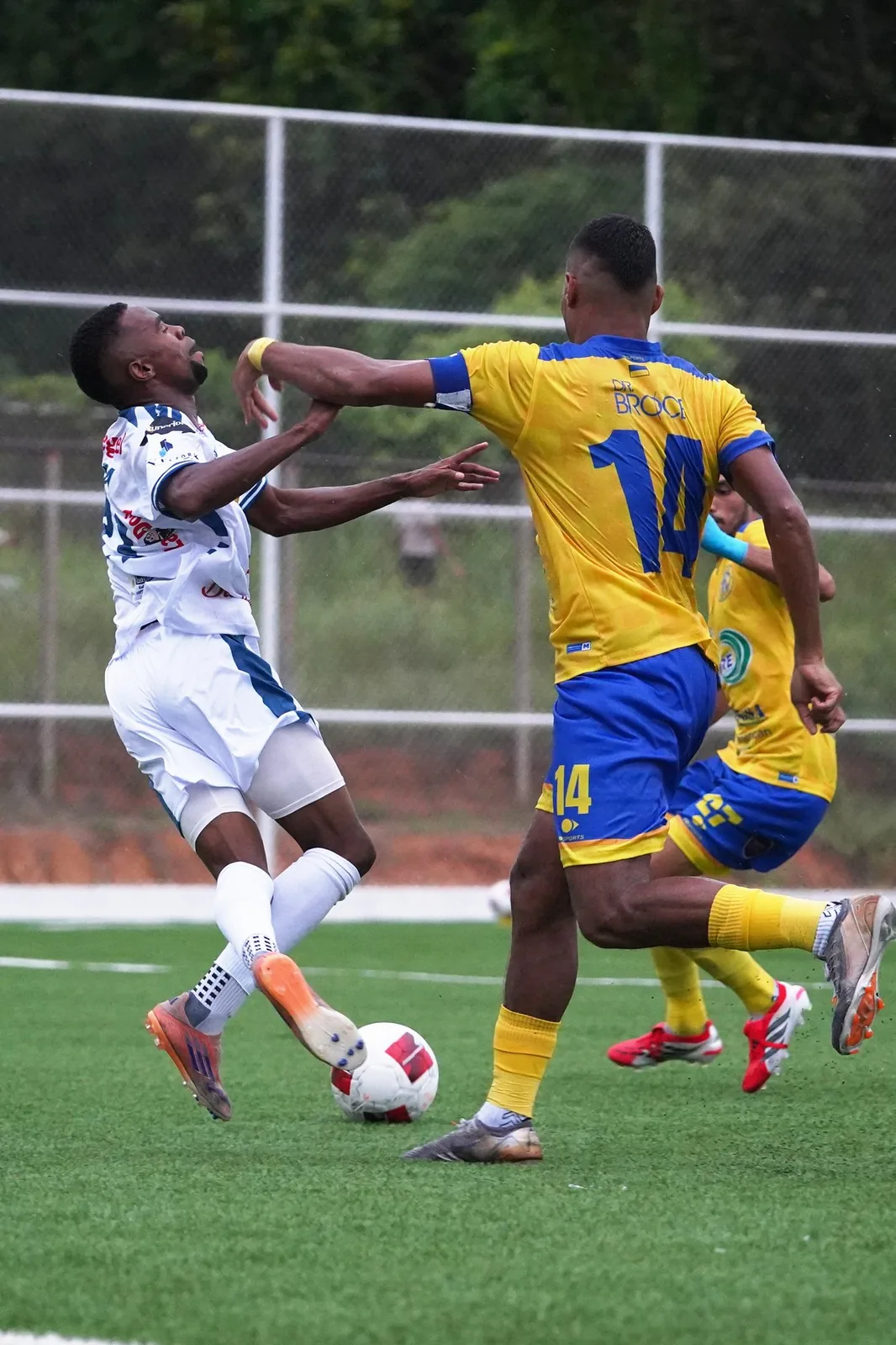 Jugador de amarillo y rival de blanco chocando por el balón
