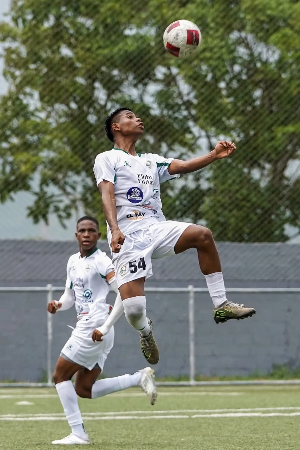 Jugador de blanco con el número 54 controlando el balón en el aire