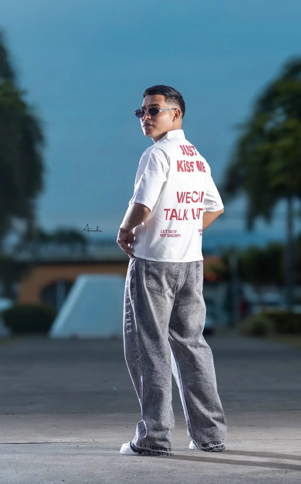 Joven de espaldas con lentes de sol y camisa blanca con letras rojas, estilo urbano