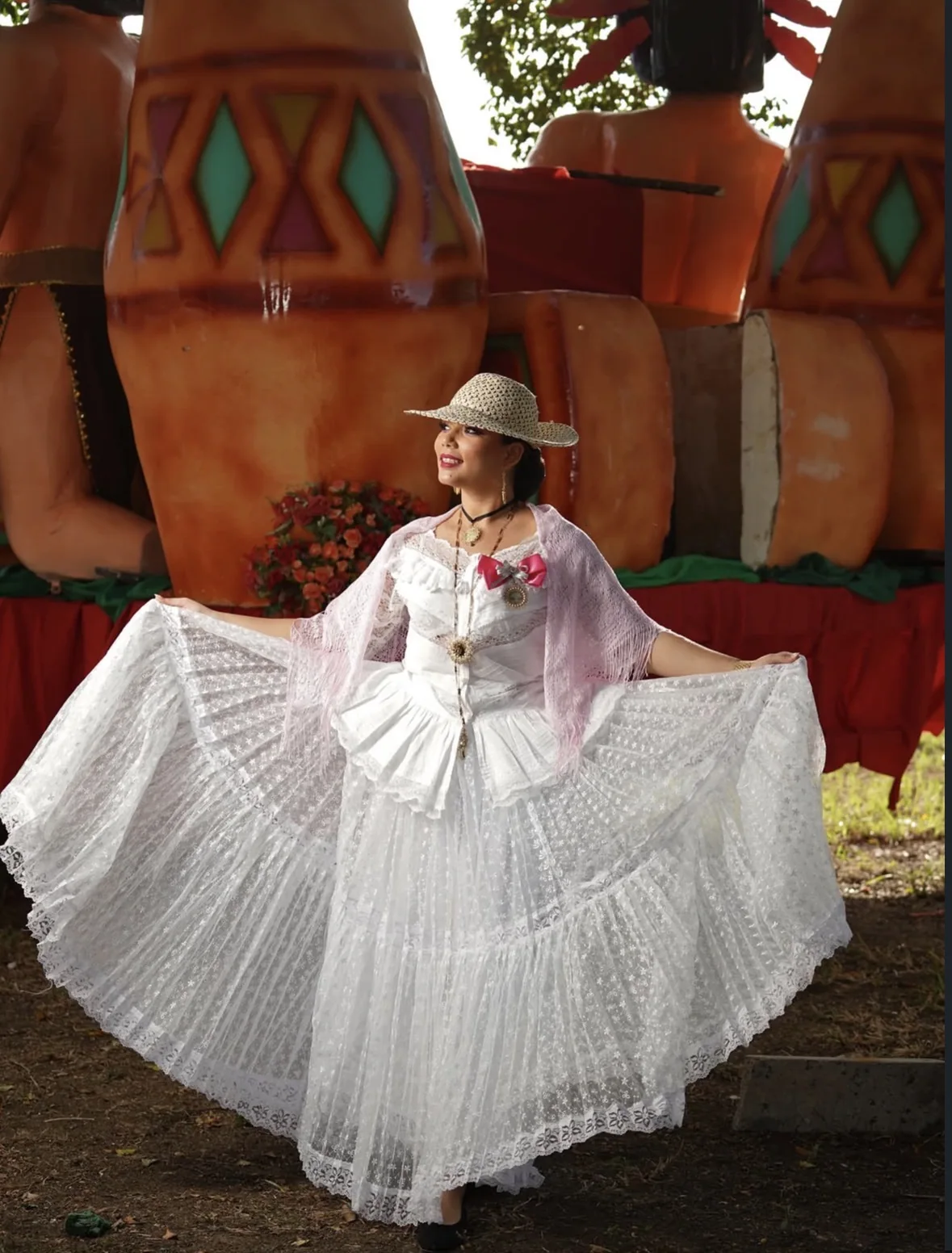 Joven con pollera blanca y sombrero de paja abriendo la falda, con figuras de carnaval al fondo